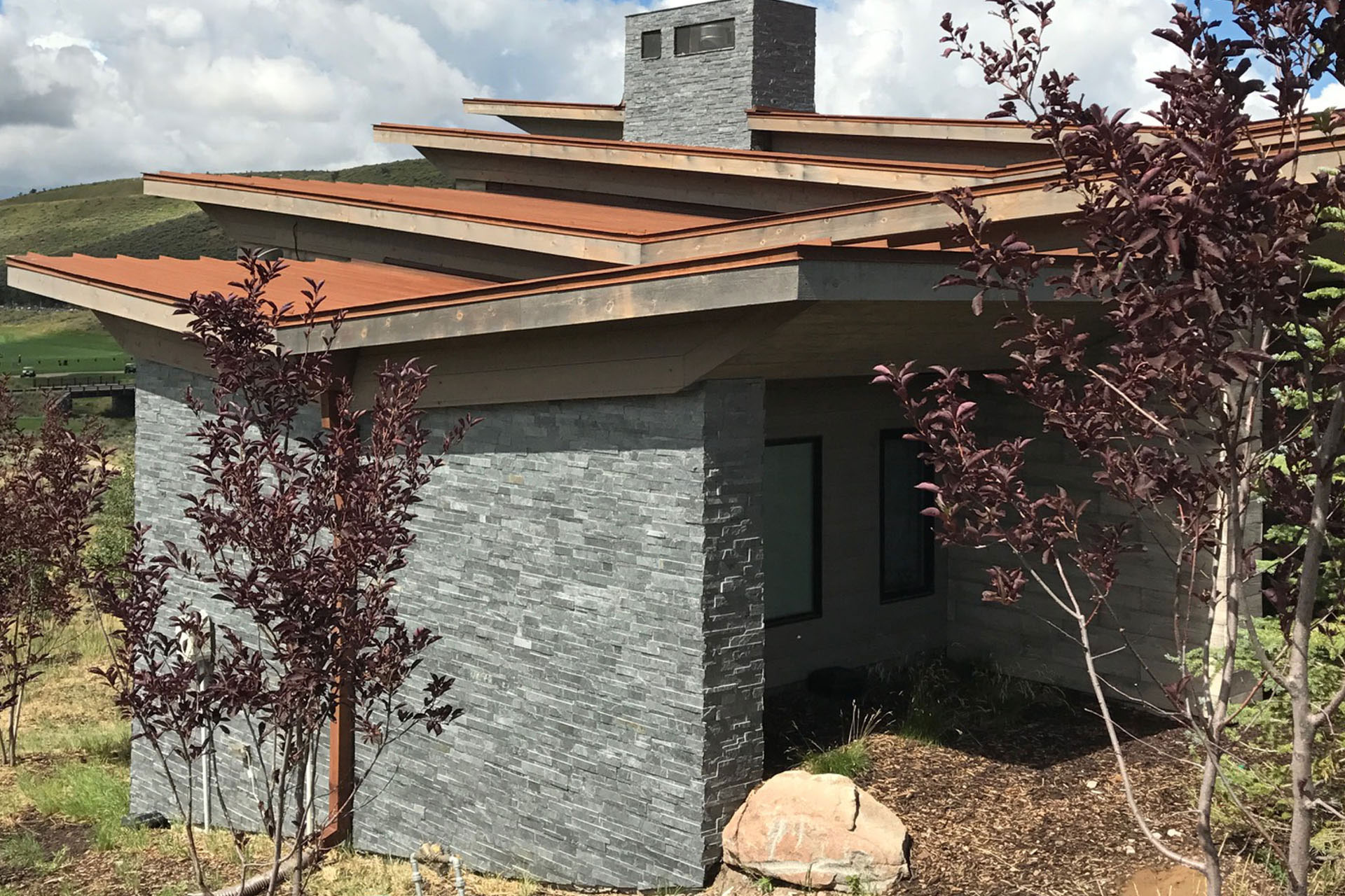 Natural stone veneer wall under a wood pergola on a modern home exterior